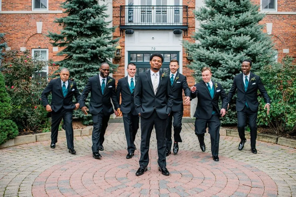 Groomsmen in black suits stride across the brick courtyard together