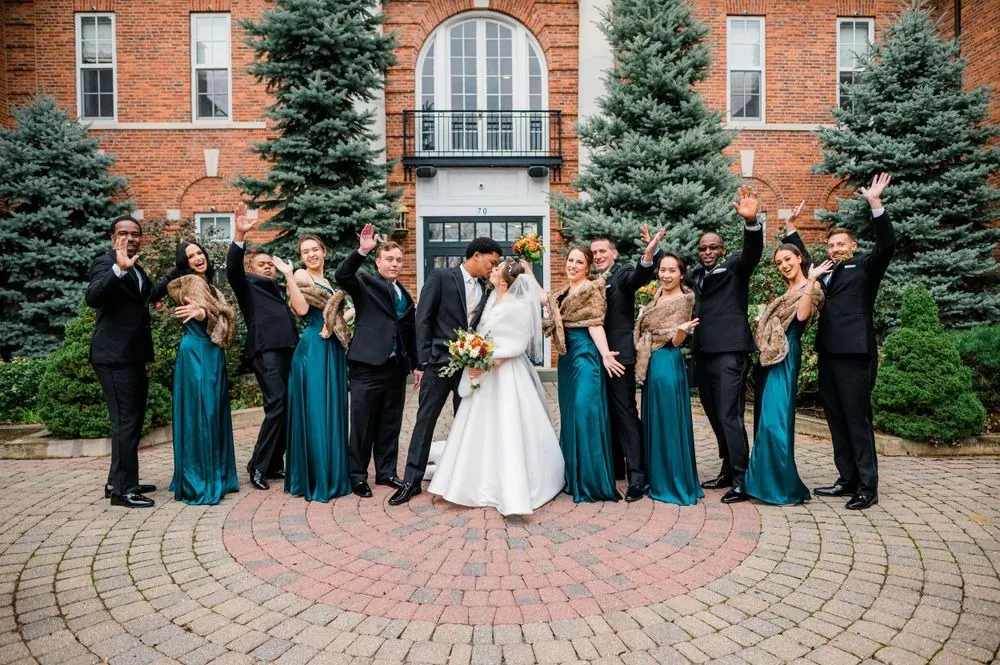 The full wedding party cheers around the couple in the brick courtyard