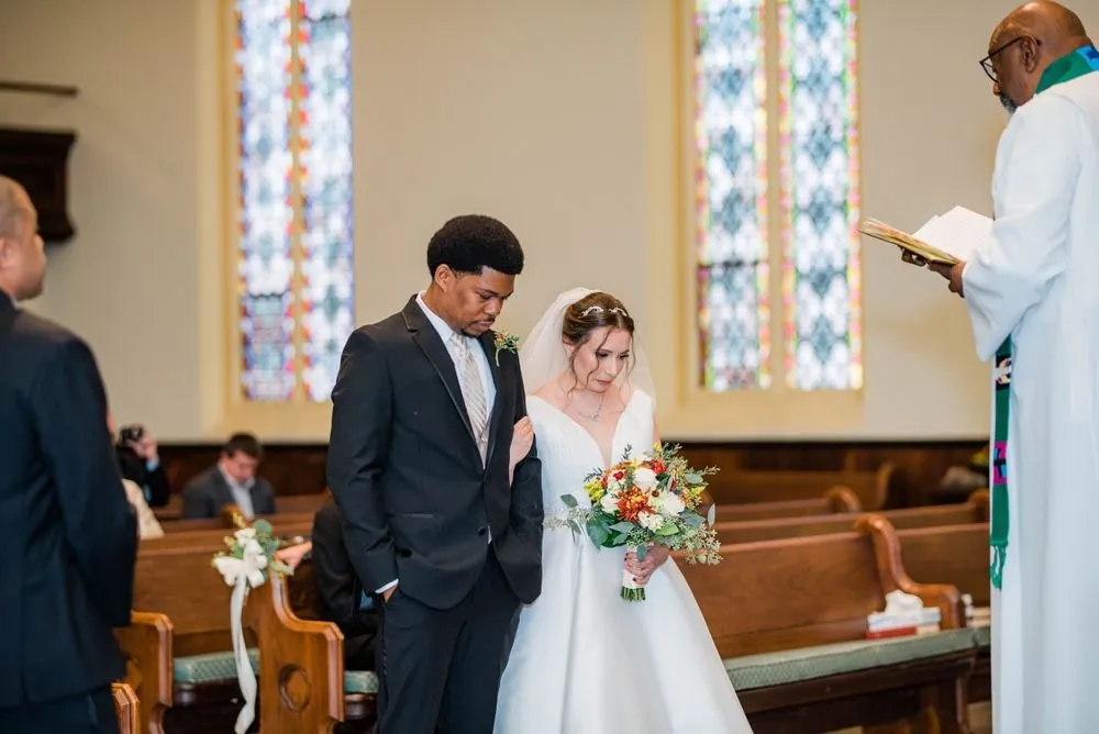 The couple stands before the officiant at the altar with stained glass behind them