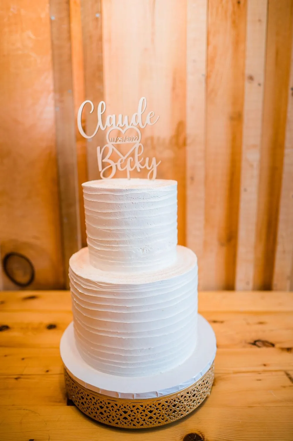A tiered white cake topped with a Claude and Becky script topper on wood