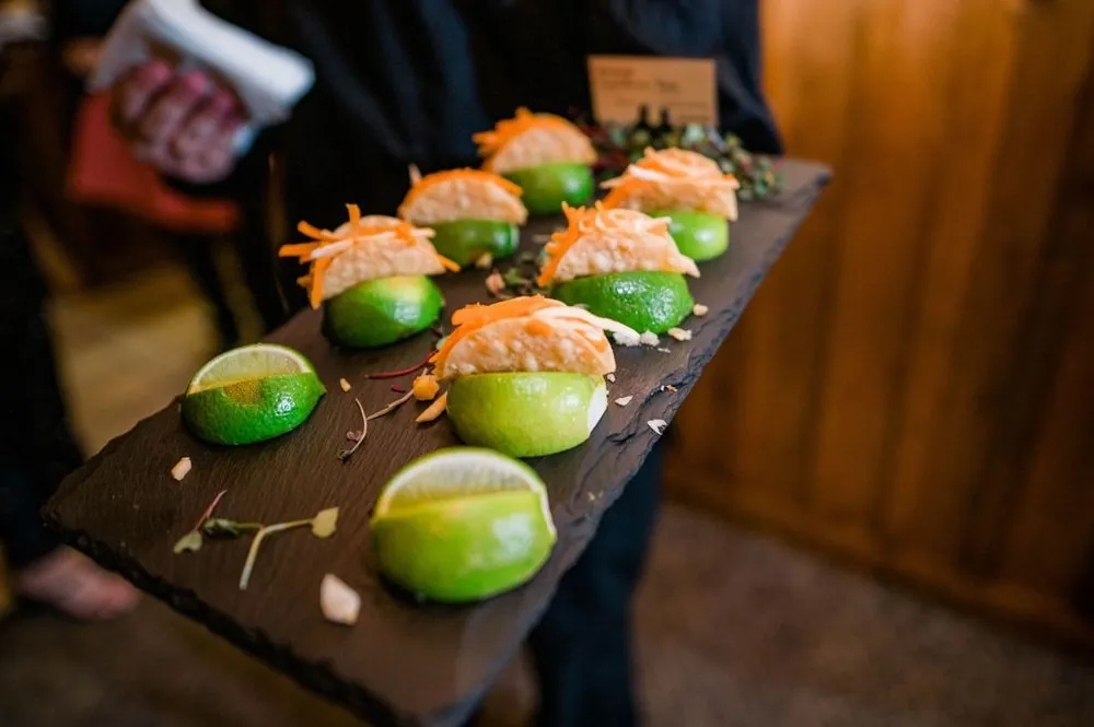 A server carries bite-sized appetizers topped with lime wedges on a slate board
