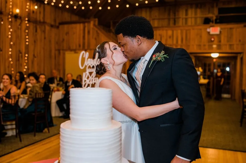 Claude and Rebecca kiss beside their white cake in the warm pavilion
