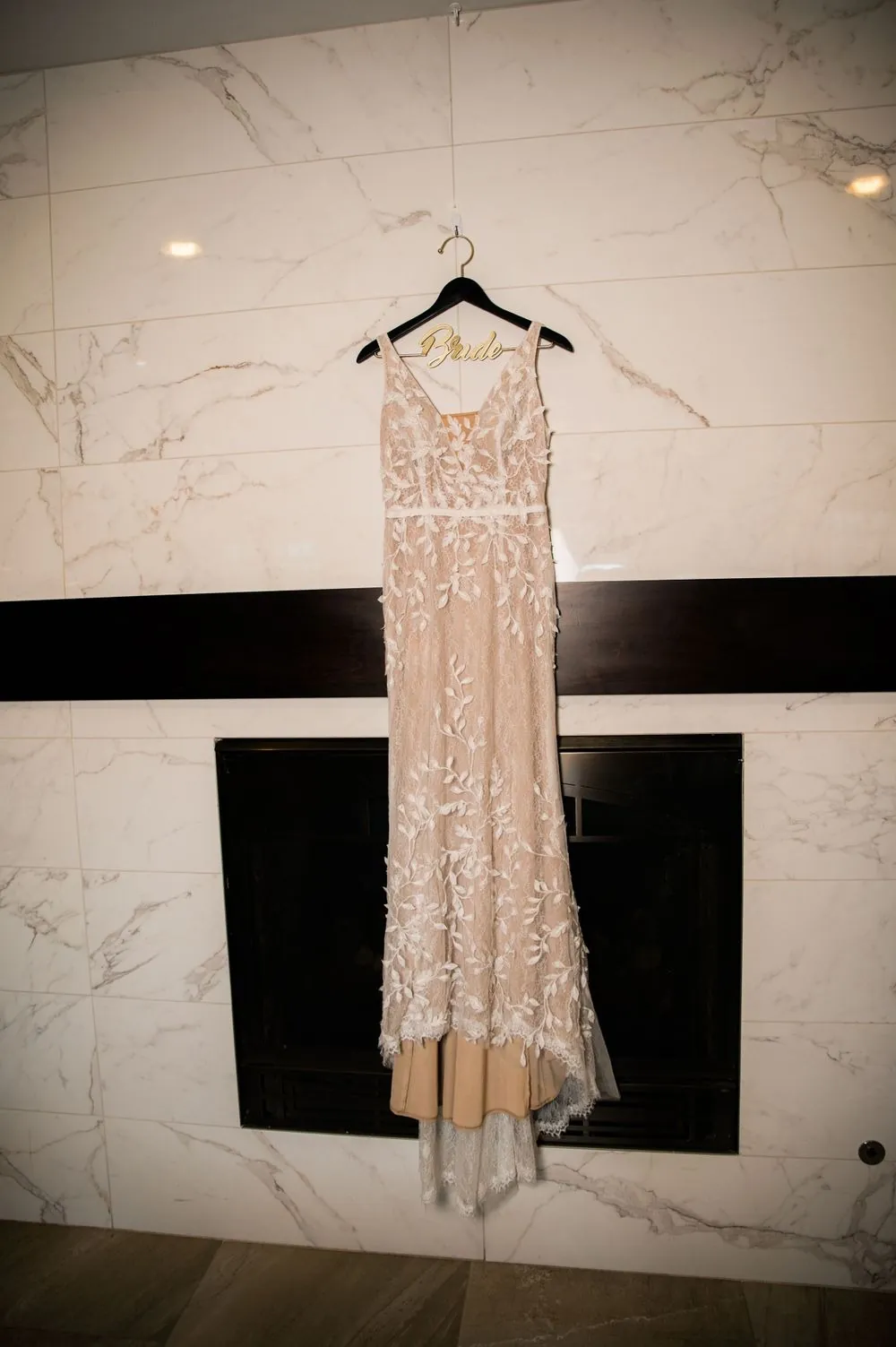 The beaded lace gown hangs on a hanger against a dark door