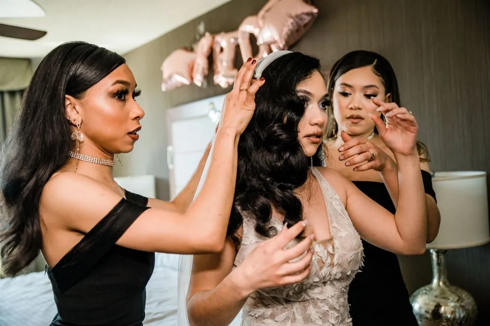 2 bridesmaids in black adjust the bride's headband and waves before the mirror