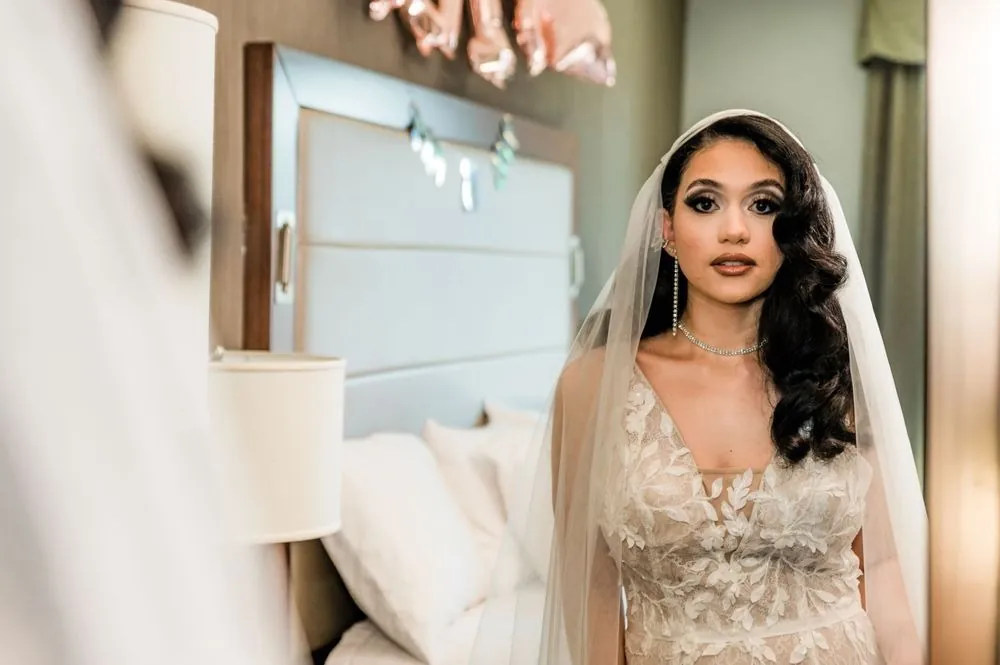 The bride in her veil and beaded gown turns toward the window light