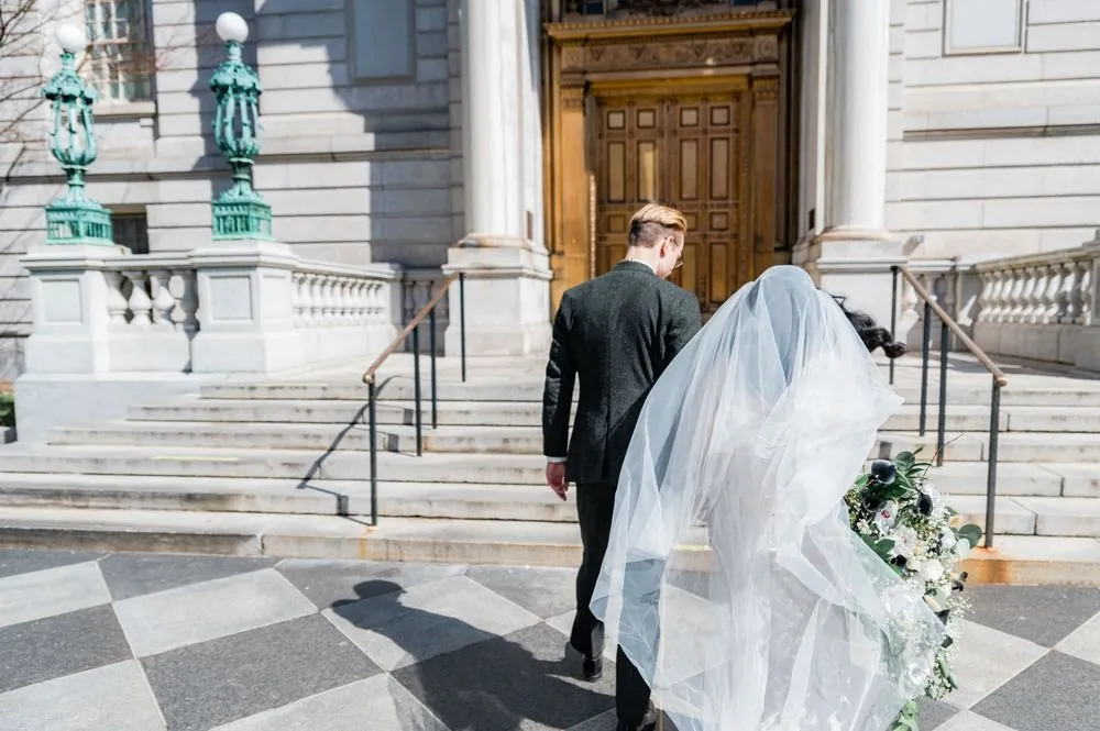 Colin and Victoria walk toward the City Hall steps, her veil trailing across the plaza