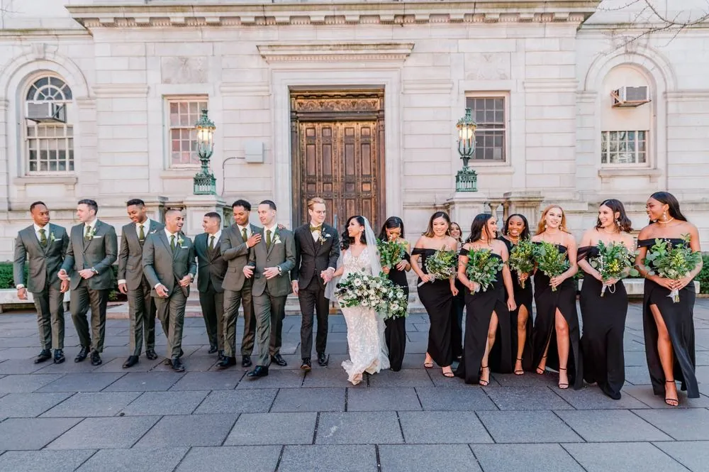 The full wedding party in black and forest green lines up before carved wooden doors