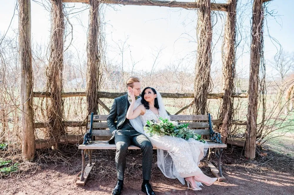 Victoria leans into Colin on a wooden bench under a rustic arbor