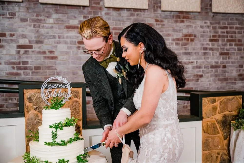 Victoria and Colin cut their greenery-wrapped cake in front of a brick wall
