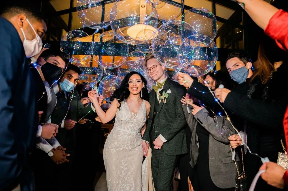 Victoria and Colin leave under glowing bubble balloons held by masked friends