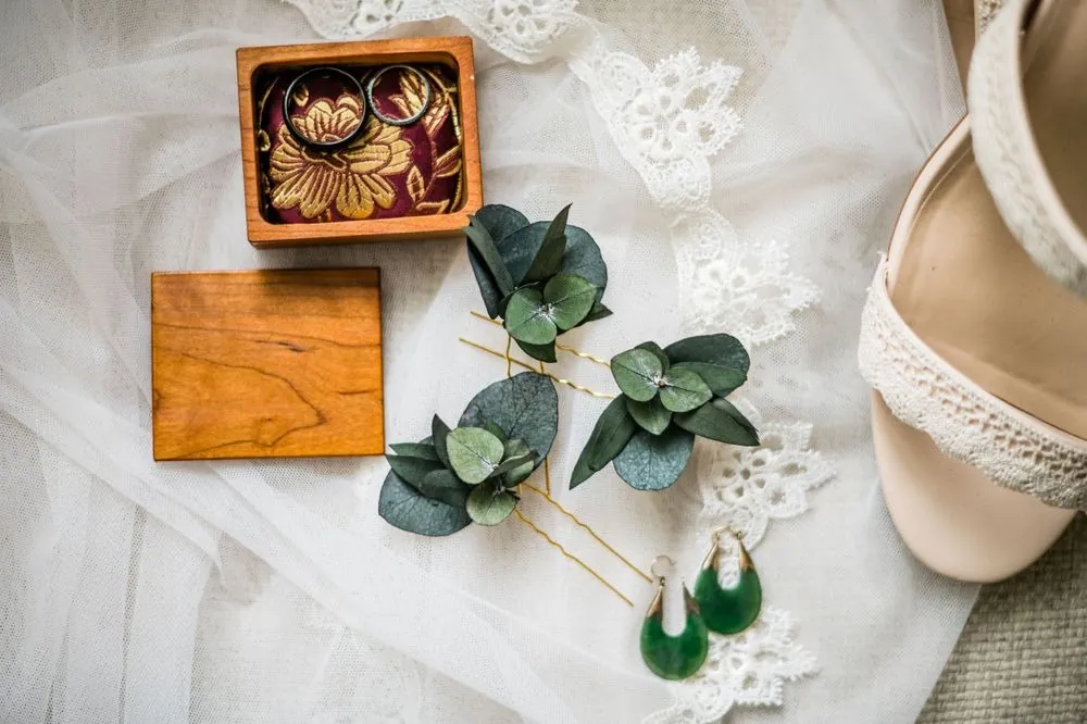 Carved wooden ring box, eucalyptus hair pins, and green stone earrings resting on lace