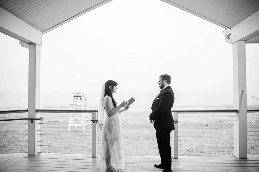 Black and white frame of Dana reading vows to Michael on the covered deck in heavy fog