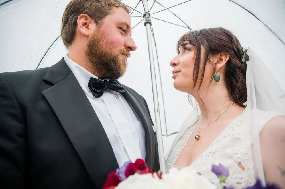 Michael and Dana look at each other under a clear umbrella, her green earrings catching light