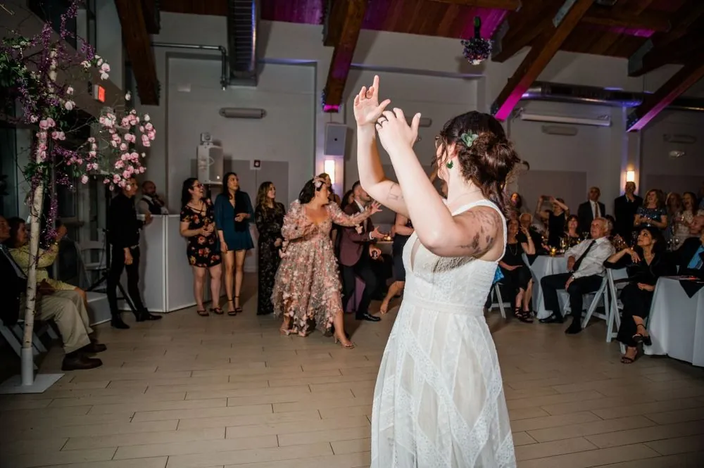 Bride throws both arms up on the dance floor as friends dance behind her
