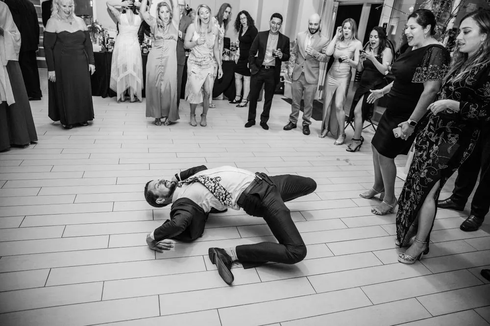 Black and white frame of a guest breakdancing on the floor inside a circle of cheering guests