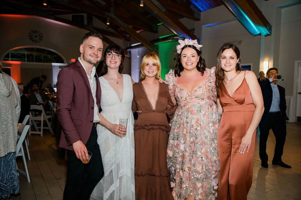 Bride poses with friends in rust and floral dresses under colored reception lights