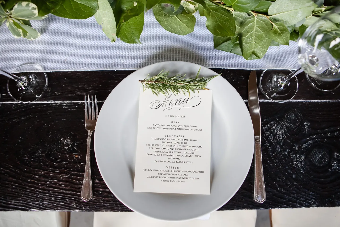 A menu card under a sprig of herbs on a white plate at a dark wood table