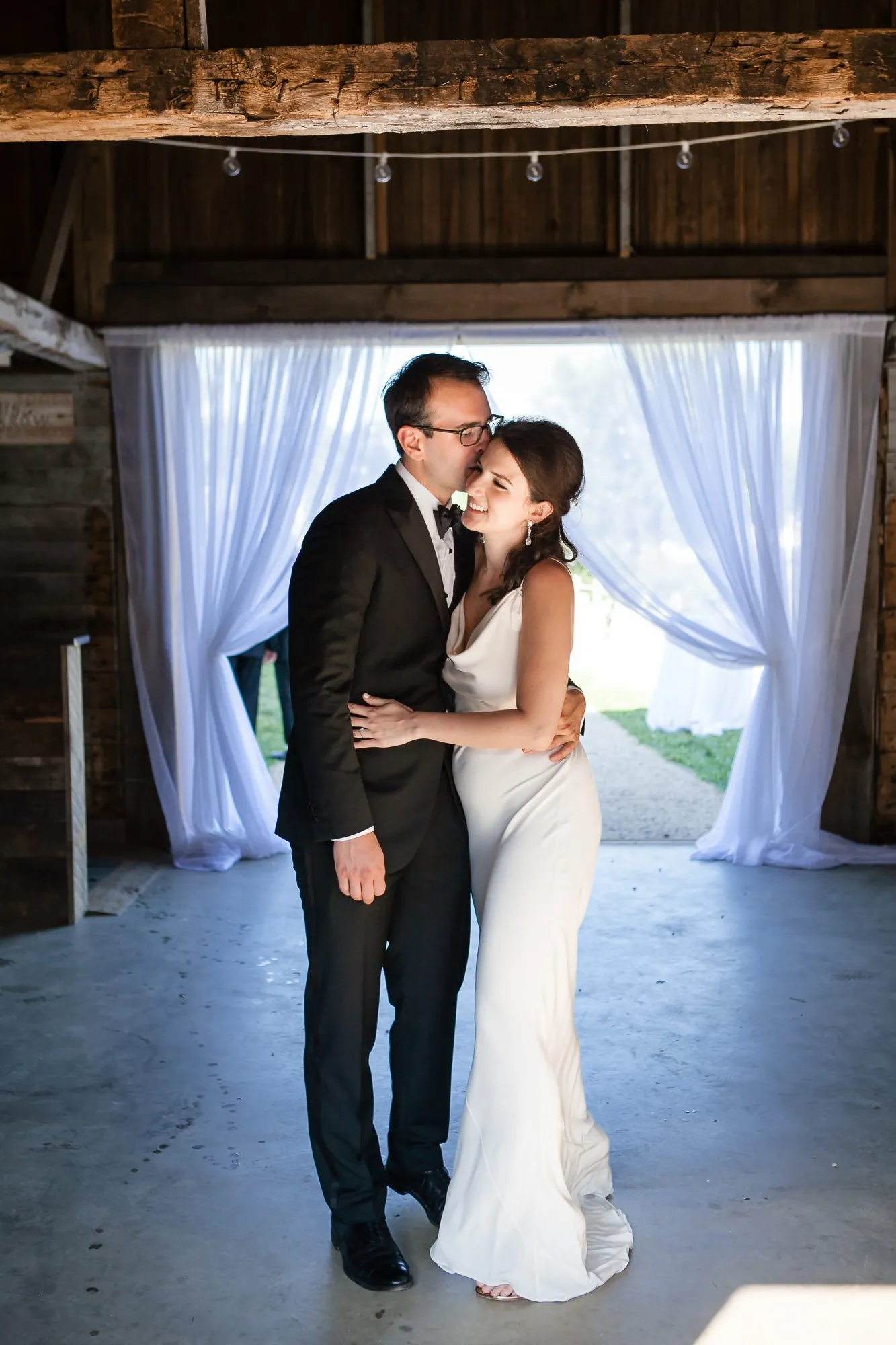 EJ and Alex embrace in the barn doorway between white curtains