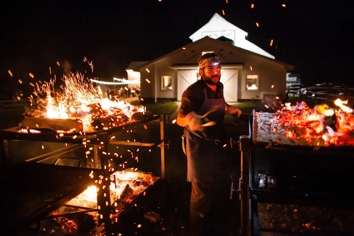 Flames and sparks rise from the grill as a cook works in the dark