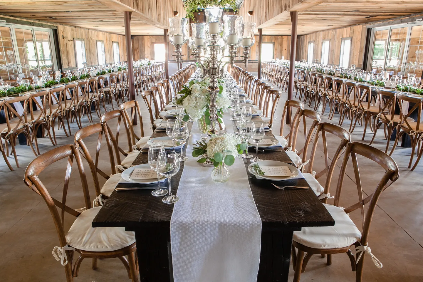 Long dark wood tables with white runners and cross-back chairs fill the barn