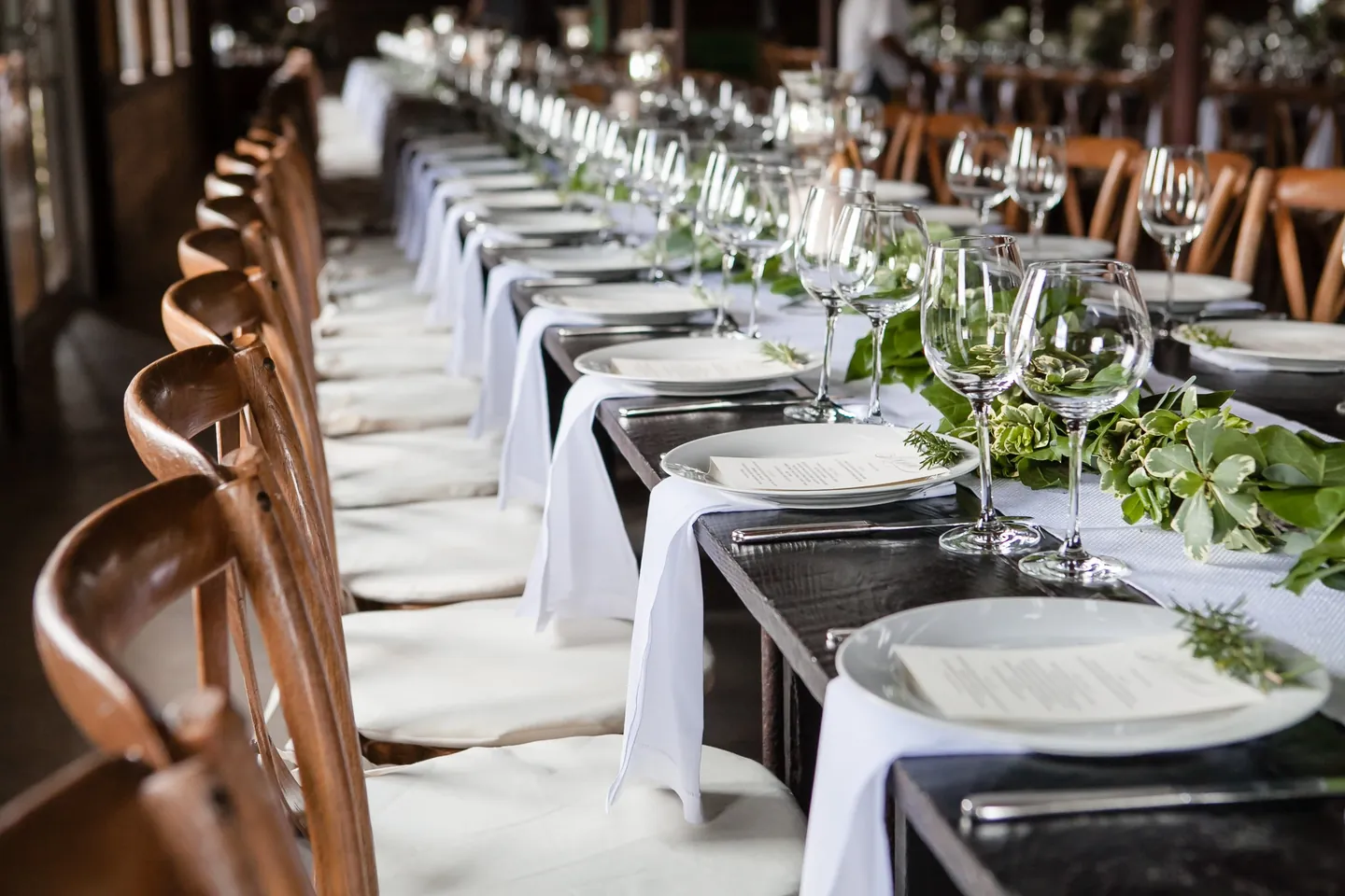 White plates, eucalyptus garland, and glassware down a long barn table