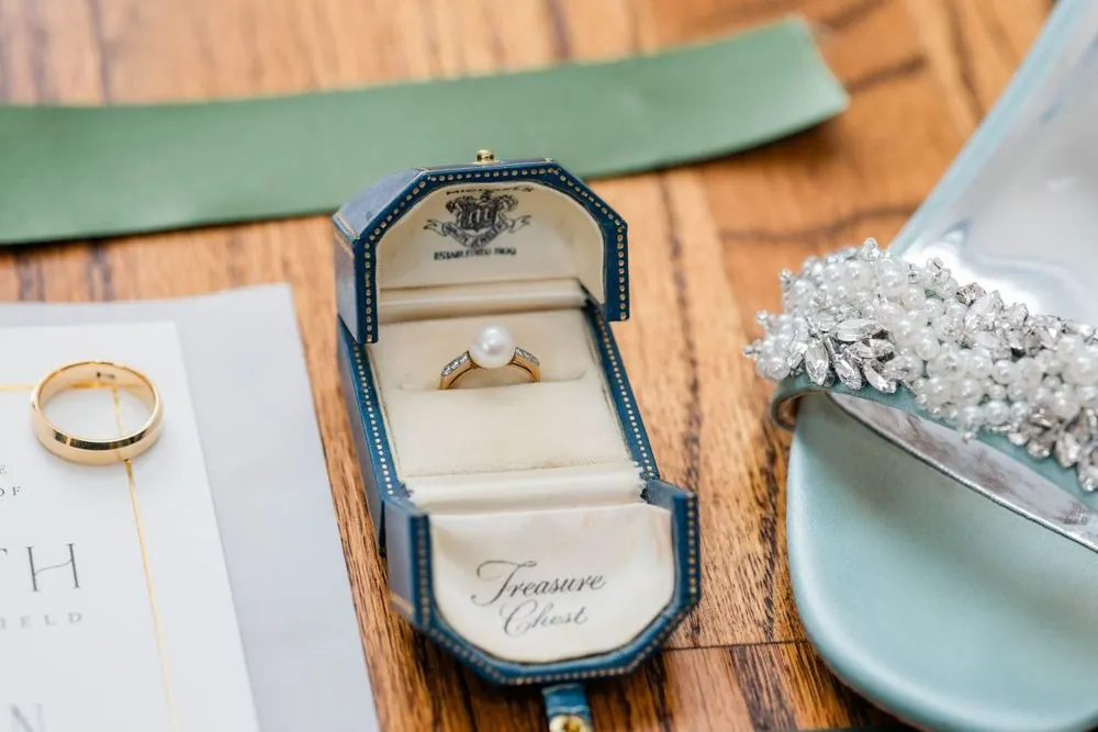 Wedding bands and an engagement ring in a velvet box on a wooden tray beside green ribbon