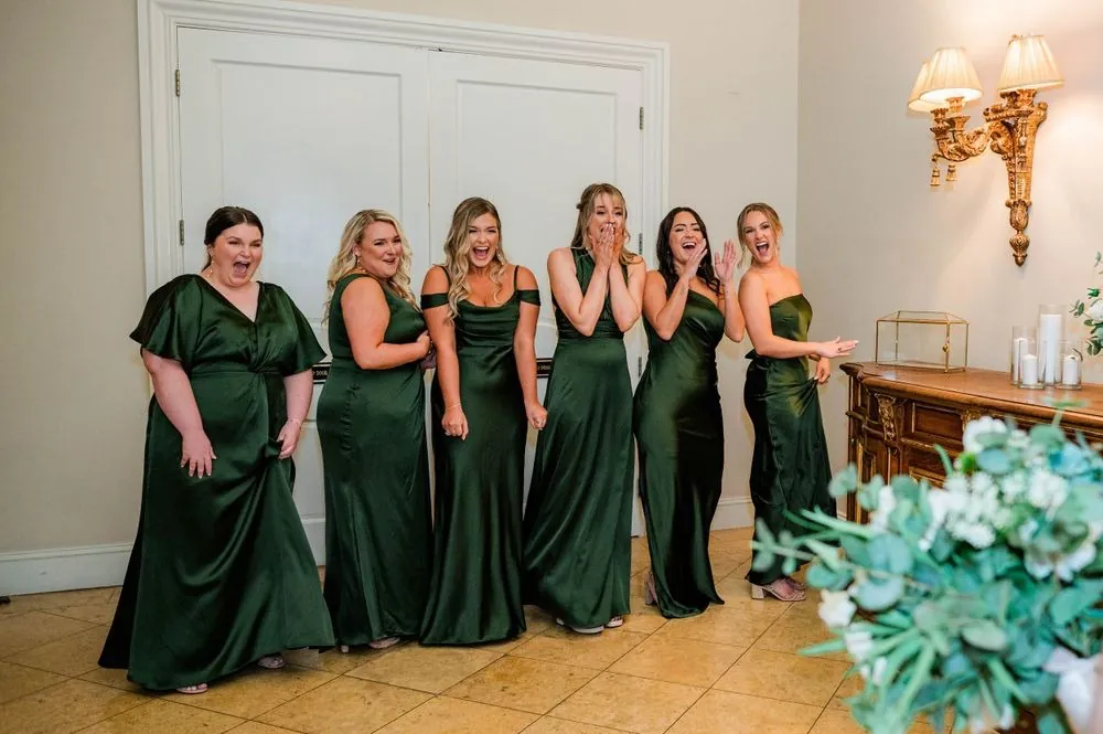 Bridesmaids in long emerald dresses react as they see the bride for the first time