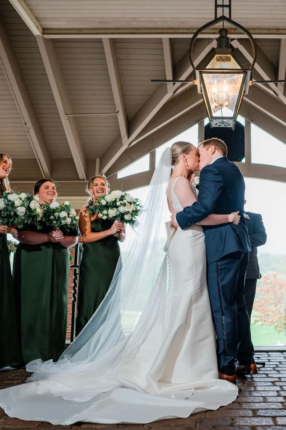 The couple shares their first kiss beneath the porch lantern as the wedding party watches