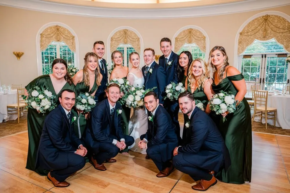 The full wedding party crowds around the couple inside the round arched ballroom