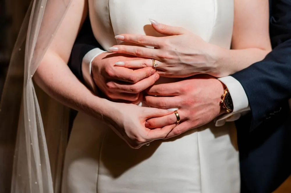 Close view of the groom's hands wrapped around the bride's waist, showing both rings