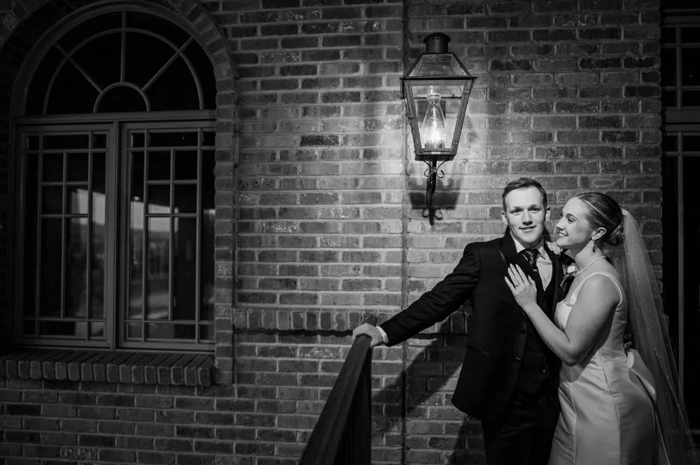 Black and white portrait of the couple laughing against a brick wall beside a lantern at night
