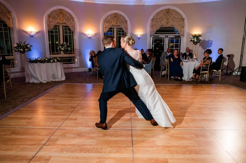 The groom dips the bride low during their first dance on the wooden ballroom floor