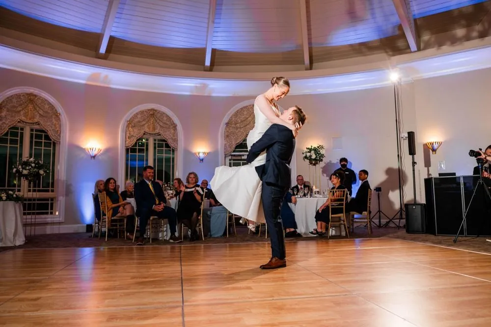 The groom lifts the bride off the floor mid first dance as guests watch from their tables