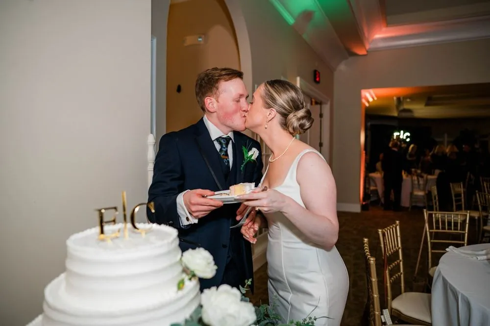 The couple shares a kiss after cutting a tiered white cake with a monogram topper