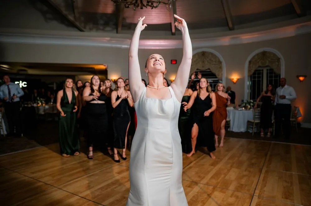 The bride raises her bouquet overhead before the toss as guests gather behind her