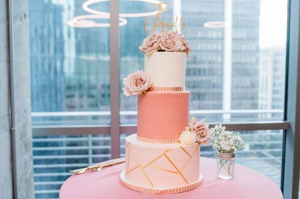 A tiered pink and white cake with gold lines against the downtown skyline