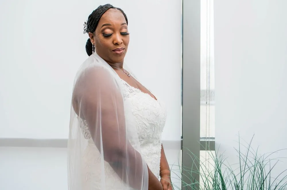 The bride in her veil looks down in soft window light before the ceremony
