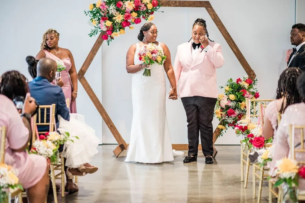 Erin and Sheretha walk back up the aisle hand in hand, smiling at guests