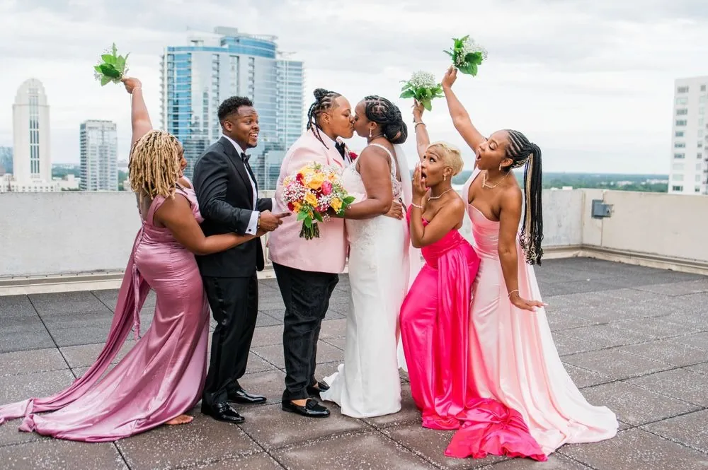 The wedding party throws bouquets in the air on the rooftop against the skyline