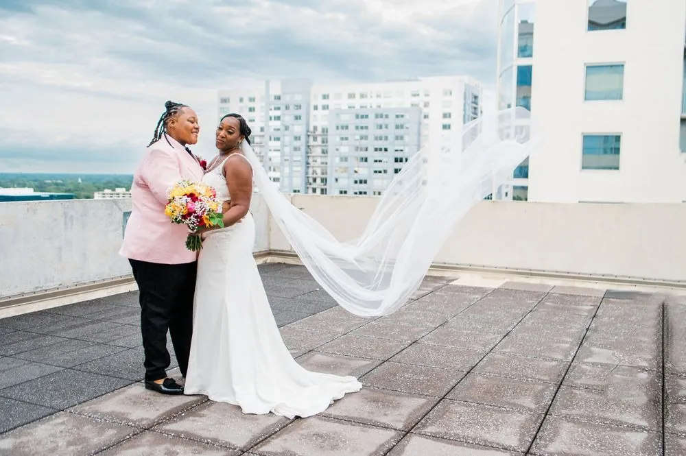 Erin and Sheretha embrace on the rooftop as the wind carries the long veil sideways