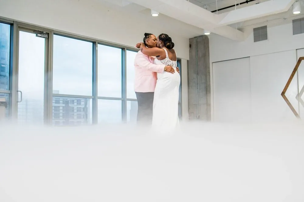 The couple dances in a cloud of low fog beside tall windows