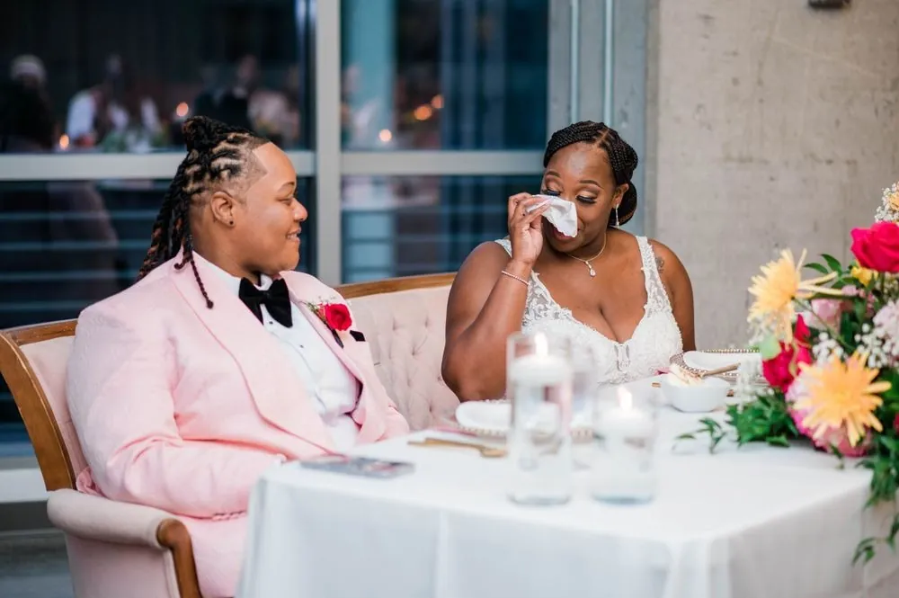 The couple laughs and wipes away tears at their table during toasts