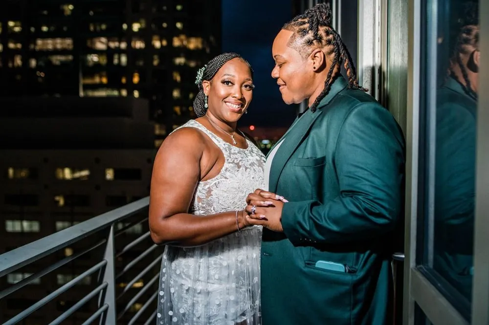The couple in evening outfits holds hands on the balcony at night