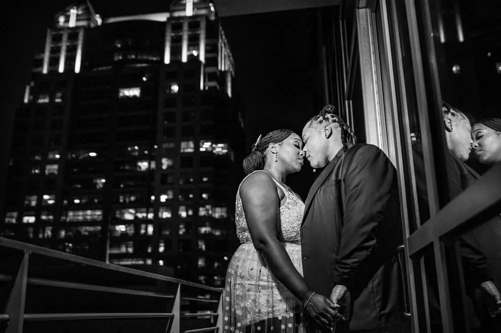 Black and white frame of Erin and Sheretha about to kiss on the balcony, lit towers behind