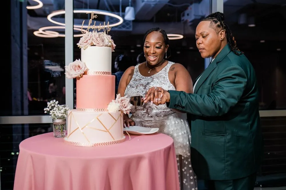 The couple cuts the tiered pink cake, one of them now in an emerald suit