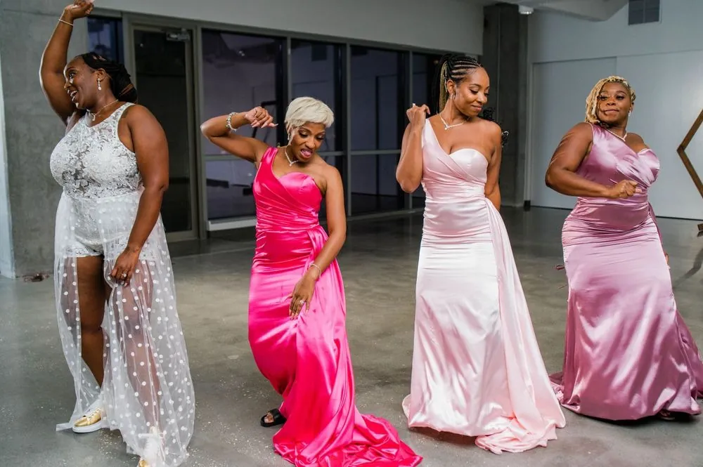 Bridesmaids in pink satin dance with the bride in a short lace dress