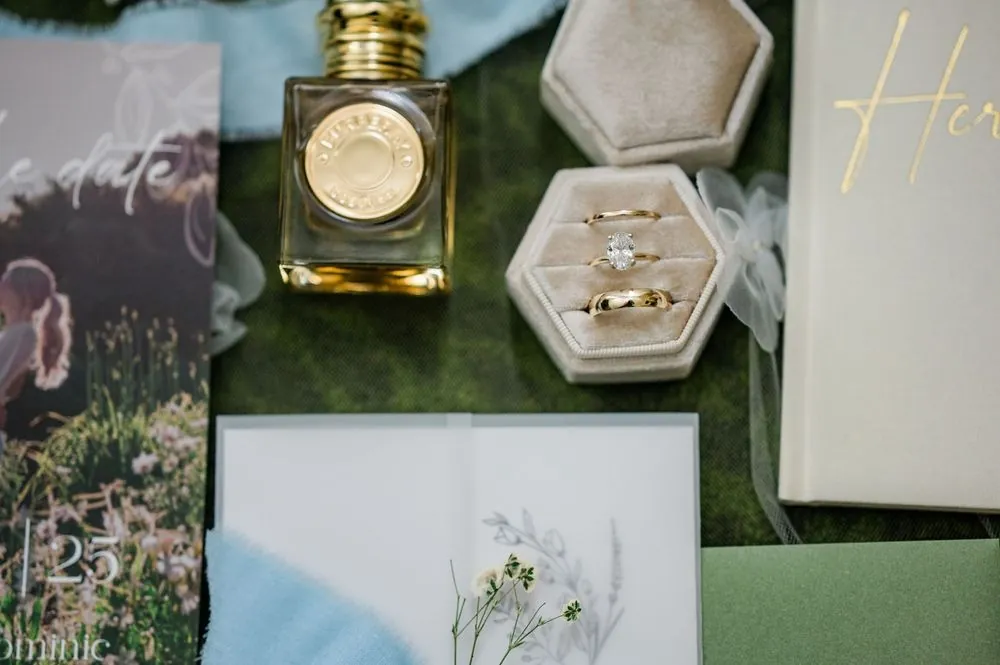 Perfume bottle, velvet hexagon ring box and invitation cards on green fabric