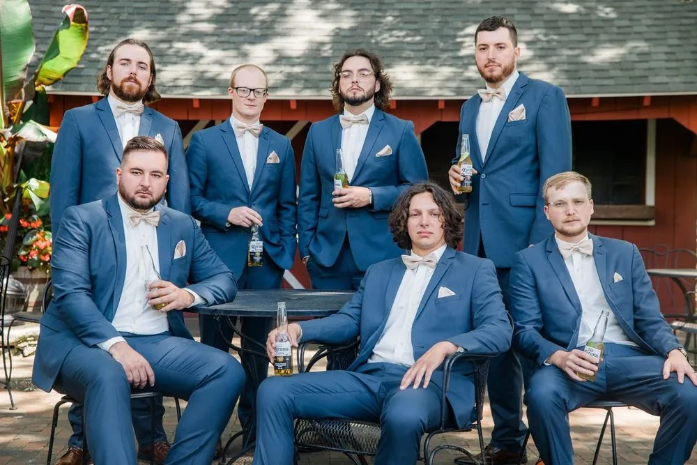 Groomsmen in blue suits lounge together on a patio outside a red building