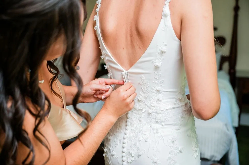 Close view of hands fastening the row of buttons down the bride's back