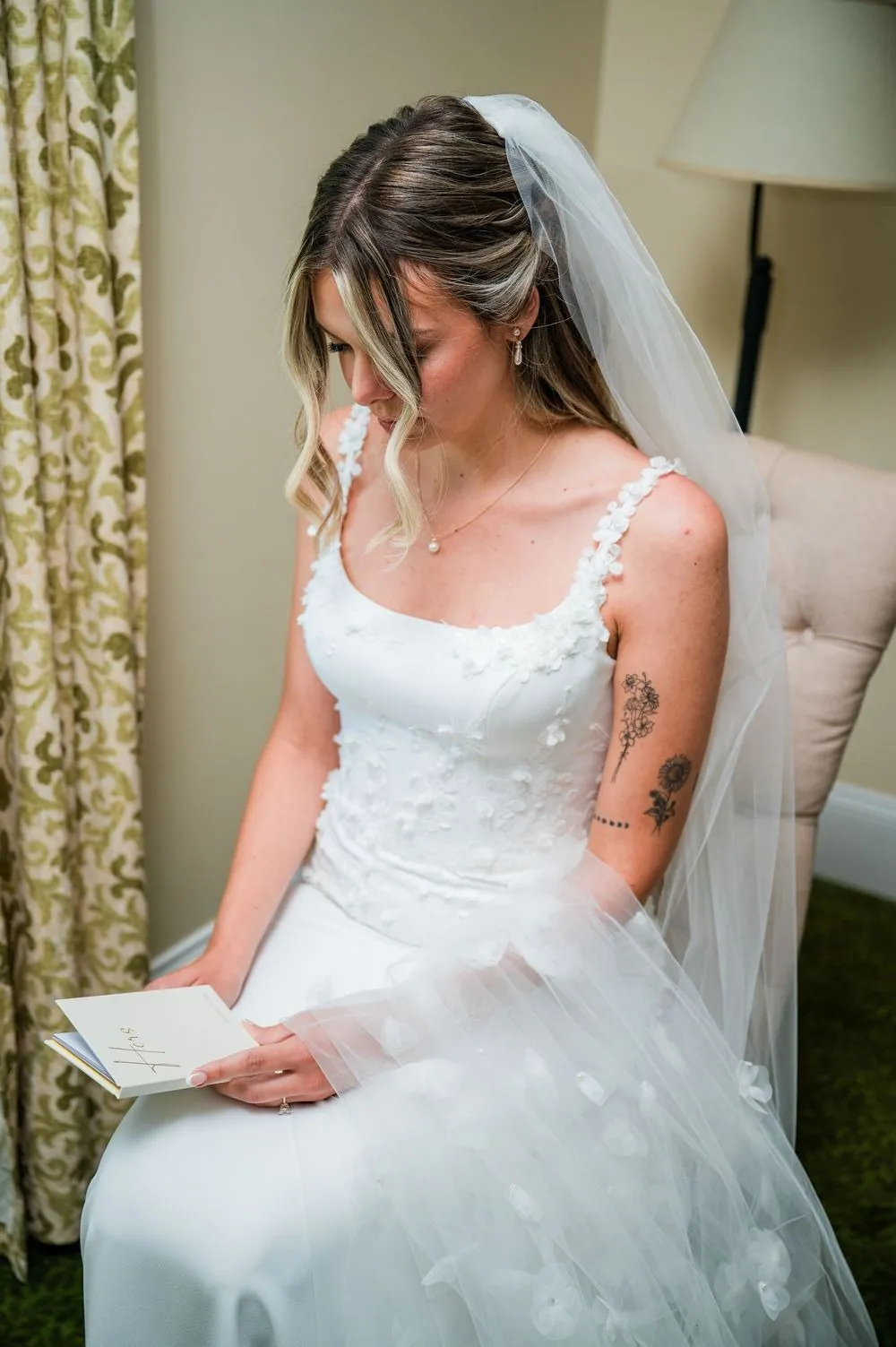 The bride reads a letter by the window in her gown and veil